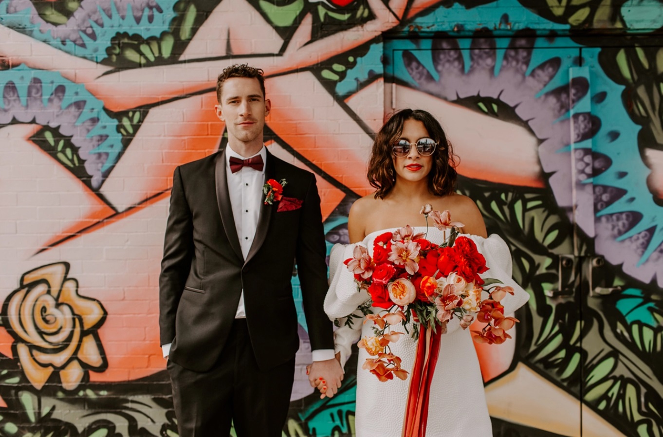 Bruid met zonnebril op voor een gekleurde muur